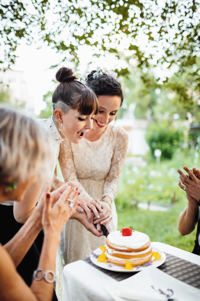 Two brides celebrating their wedding in Galway, cutting their cake outdoors surrounded by friends and family during an intimate LGBTQ+ ceremony.